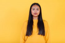 Porträt einer Asiatin, die auf gelbem Hintergrund im Studio steht und in die Kamera blickt — Stockfoto