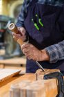 Trabajador de madera masculino irreconocible con martillo de madera y cincel tallado detalle de madera mientras trabaja en taller de carpintería profesional - foto de stock