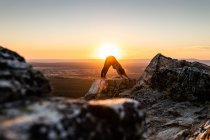 Молодая женщина йога практикует йогу на скале в горах со светом восхода солнца, вид сбоку — стоковое фото