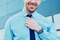 Crop unrecognizable smiling bearded male executive in formal shirt and tie in city on blurred background — Stock Photo