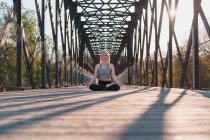 Рівень жіночої статі з закритими очима, що сидять в позі Падмасани під час практики йоги на мостовому шляху при сонячному світлі. — стокове фото