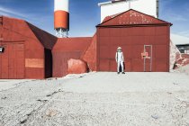 Людина в космосі стоїть біля червоної стіни промислового об'єкта в сонячний день — стокове фото