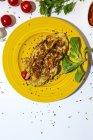 Deliciosa tortilla con perejil picado en plato contra tomates secados al sol sobre fondo blanco - foto de stock