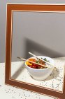 High angle of white bowl with tasty poke dish and chopsticks placed behind frame on table covered with sesame seeds — Stock Photo