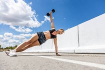 Jeune femme de formation avec son haltère à l'extérieur, haltère flexion et bras levé, vue latérale — Photo de stock
