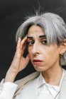Впевнена стильна транссексуальна жінка з сірим волоссям торкається голови в місті вдень — стокове фото