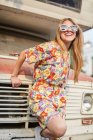 Fröhlich-selbstbewusste Frau im trendigen Sommeranzug steht neben alten verlassenen Wohnwagen und blickt in die Kamera — Stockfoto