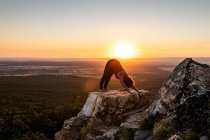 Junge Yogi-Frau praktiziert Yoga auf einem Felsen im Gebirge im Licht des Sonnenaufgangs, Seitenansicht — Stockfoto
