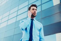 From below stylish male executive in formal clothes talking on cellphone while looking away in town — Stock Photo