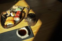 З верхньої тарілки з асортовані суші рулони подають на столі з паличками для їжі і соєвим соусом в японському ресторані. — стокове фото