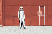 Hombre en traje espacial de pie cerca de la pared roja de la instalación industrial en el día soleado - foto de stock