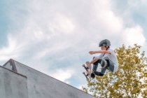Adolescent garçon saut avec skateboard et montrant cascade sur rampe dans skate park — Photo de stock