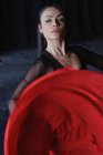 Молодая женщина с макияжем в красной и черной одежде исполняет традиционный испанский танец, глядя в камеру — стоковое фото
