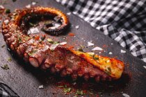 From above delicious grilled octopus tentacle served with spices on wooden board on checkered cloth — Stock Photo