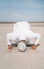 Нерозпізнаний мусульманин, який стає навколішки на килимі і торкається землі чолом під час молитви на піщаному березі в сонячний день. — стокове фото