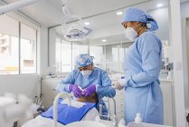 Stomatologin in Uniform und Atemmaske heilt Zähne eines männlichen Patienten im Krankenhaus — Stockfoto