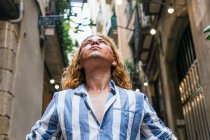 From below peaceful unemotional male with long hair standing in street and enjoying freedom while looking away — Stock Photo