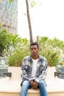 Unbeweglicher Afroamerikaner sitzt auf Bank mit Steckdosen für Ladegeräte in der Stadt und schaut weg — Stockfoto