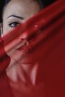 Crop junge Frau mit roten Lippen blickt in die Kamera hinter transparentem Textil mit Falten — Stockfoto