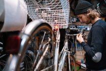 Vista lateral de la bicicleta de fijación maestra masculina ocupada mientras se trabaja en taller de reparación en mal estado - foto de stock