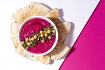 Draufsicht auf appetitliche Rote-Bete-Hummus garniert mit Kichererbsen auf zwei farbigen Hintergrund mit Brot serviert — Stockfoto