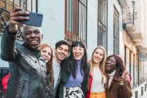 African American male taking selfie with smartphone with company of multiracial friends standing on street together — Stock Photo