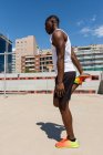 Vista lateral do atleta masculino preto apto esticando as pernas enquanto aquece os músculos antes do treino no chão de esportes no dia ensolarado — Fotografia de Stock
