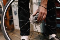 Crop anonymous male mechanic with dirty hands fixing gear cassette of wheel in repair workshop — Stock Photo