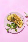 Tasty omelette on plate against fresh parsley sprigs with garlic cloves on pink background — Stock Photo