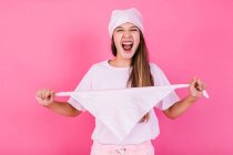 Unbekümmerte weibliche Jugendliche in lässiger Kleidung mit braunen Haaren und Kopftuch stehen für Konzeptbewusstsein und schauen in die Kamera, die auf rosa Hintergrund steht — Stockfoto