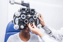 Оптометрист настраивает оптическое оборудование во время исследования зрения чернокожей женщины — стоковое фото