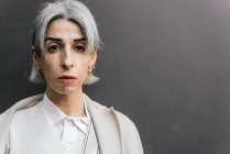 Femme transgenre élégante confiante avec des cheveux gris touchant la tête en ville le jour en regardant la caméra — Photo de stock