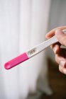 Cropped unrecognizable woman hands holding a pregnancy test besides a window — Stock Photo
