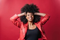 Freche Afroamerikanerin schreit und berührt Haare, während sie in die Kamera auf rotem Hintergrund im Studio schaut — Stockfoto