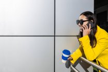 Mujer de negocios asiática con abrigo amarillo y teléfono inteligente con fondo metálico - foto de stock