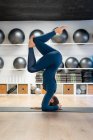 Full body side view of fit female in sportswear doing supported headstand variation pose while practicing yoga in fitness studio — Stock Photo