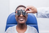 Optometrista ajustando o equipamento de optometria durante o estudo da visão de uma mulher negra — Fotografia de Stock