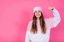 Содержание женщины-подростка в повседневной одежде и платке для концепции рака демонстрируя сильные руки, глядя в камеру с зубастой улыбкой — стоковое фото