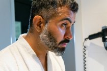 Side view of crop middle aged male in white bathrobe cleaning face with water while doing morning routine in bathroom — Stock Photo