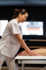 Vista lateral de feliz masajista en bata blanca masajeando ternera de cultivo mujer paciente durante la sesión de fisioterapia en la clínica - foto de stock