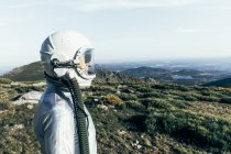 Vista lateral astronauta masculino em traje espacial e capacete em pé na grama e pedras em terras altas — Fotografia de Stock