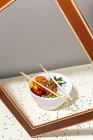 Hohe Winkel der weißen Schüssel mit leckeren Poke-Gericht und Essstäbchen hinter Rahmen auf dem Tisch mit Sesam bedeckt platziert — Stockfoto