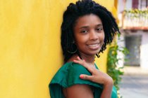 Крупним планом портрет красивої усміхненої молодої чорної жінки, що спирається на стіну зовні — стокове фото