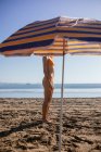 Vista laterale di anonima giovane rossa in piedi sulla spiaggia in una giornata di sole in estate — Foto stock