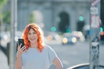 Весела руда жінка на вулиці і повідомлення в соціальних мережах на мобільному телефоні — стокове фото