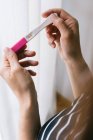 Cropped unrecognizable woman hands holding a pregnancy test besides a window — Stock Photo