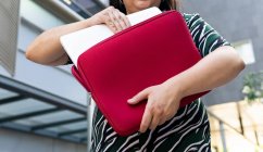 De baixo de anônimo plus size jovem estudante em roupa elegante levando laptop de caixa vermelha em fundo urbano — Fotografia de Stock