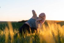 Доросла жінка в спортивному одязі практикує йогу, дивлячись вгору на луг у сонячному світлі ввечері — стокове фото