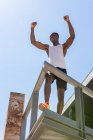 From below of African American fit male athlete standing on terrace with firsts up and celebrating victory while enjoying triumph — Stock Photo
