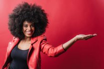 Приємна афроамериканська жінка, яка слухає музику в навушниках і користується мобільним телефоном, танцюючи на червоному тлі у студії. — стокове фото